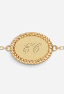 TAYLR gold oval rope bracelet with engraved initials on a polished surface and delicate chain links